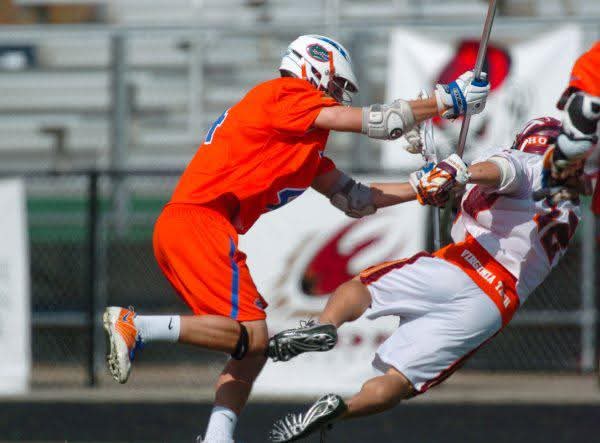 A player in orange and blue delivering a check to an opponent in a college club lacrosse game